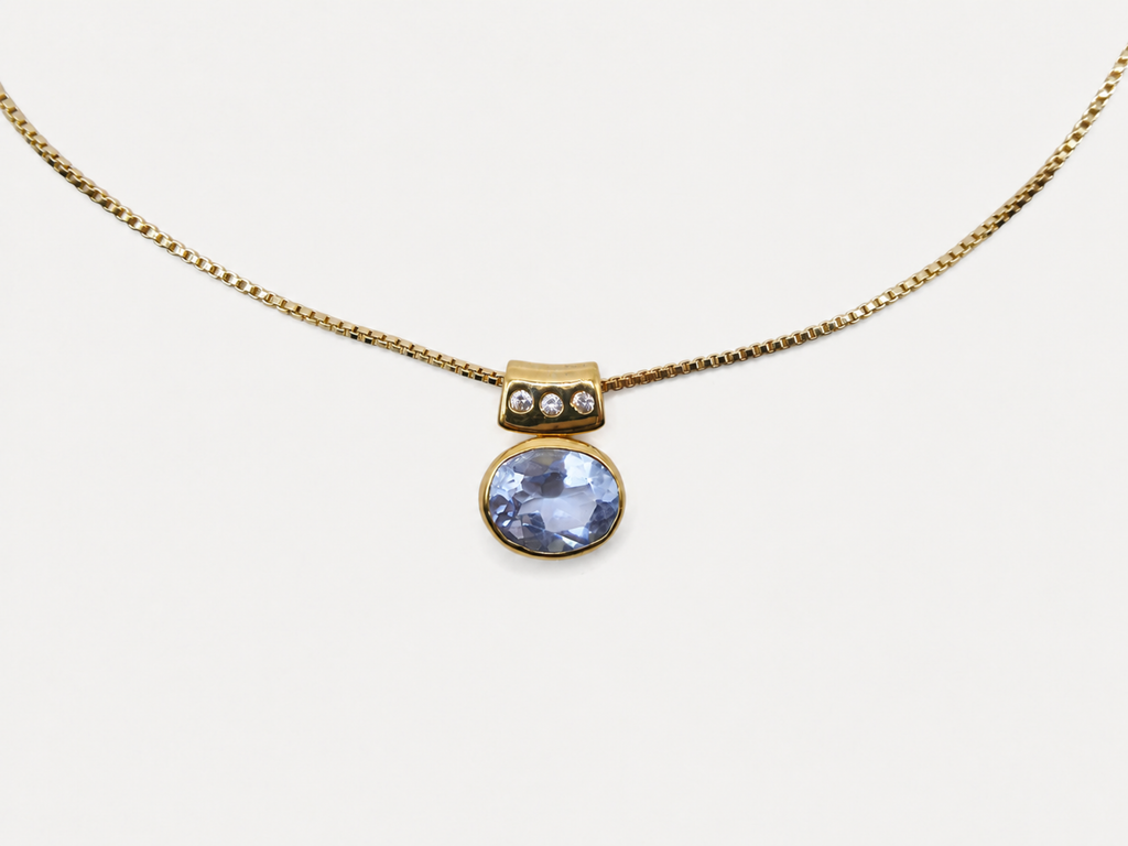 A gold chain necklace with a pendant featuring a round light blue gemstone and a small gold cap with three tiny clear stones, shown on a plain light background.